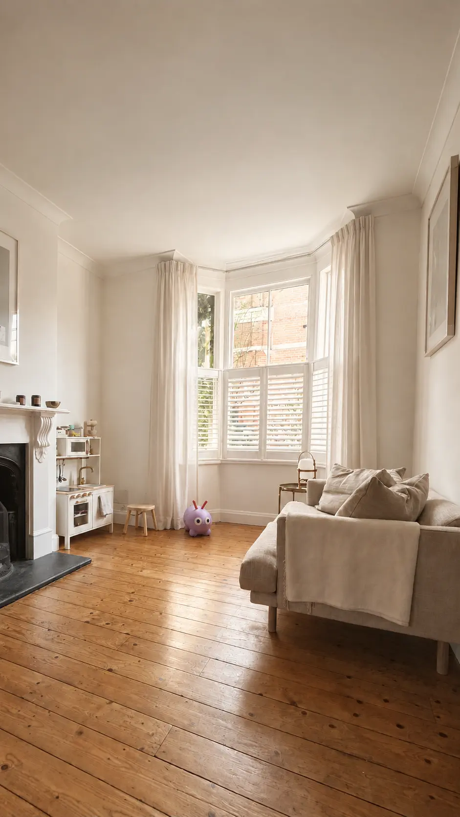 Living room of the London townhouse with bay window, pale curtains and timber floor