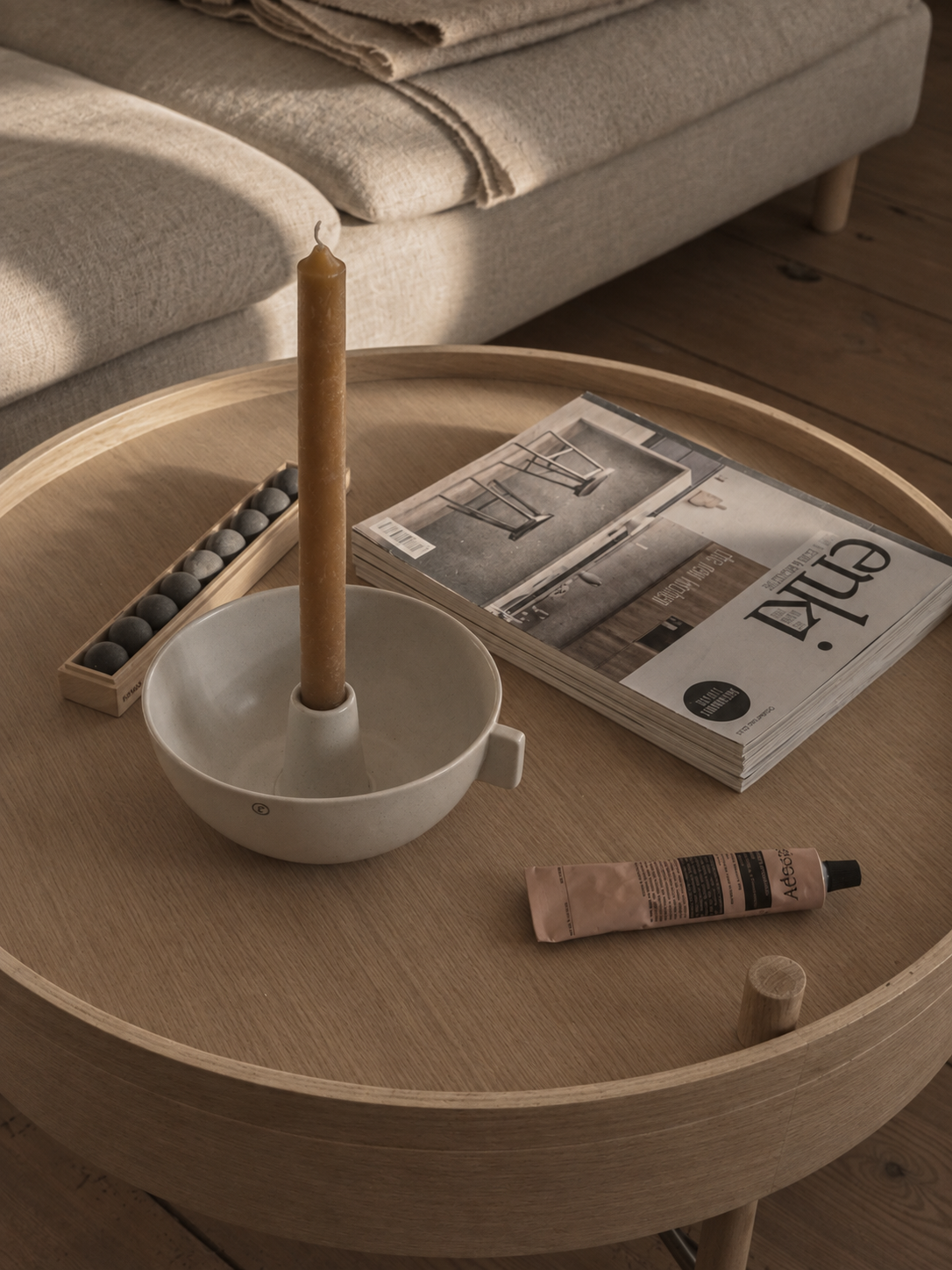 Round timber coffee table with candle and reading material beside a linen sofa in the Brandenburg home