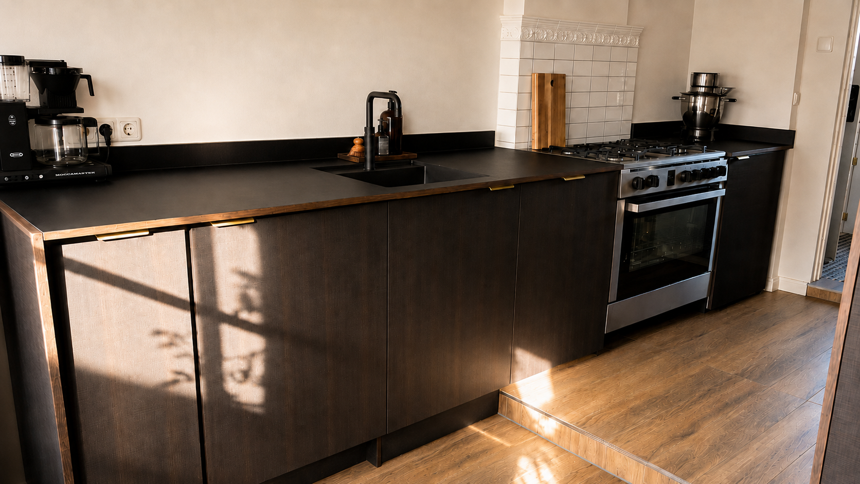 Dark kitchen cabinetry and worktop in the Brandenburg home with sunlight across the floor