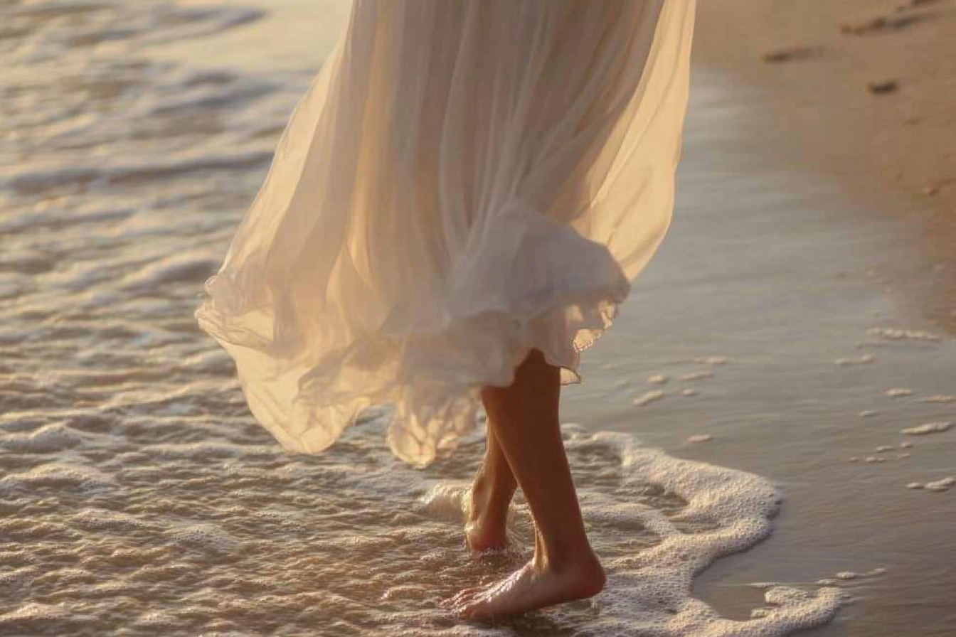 Woman in a flowing dress walking along the shoreline in soft golden light, illustrative of the feeling planned for CELANT retreats